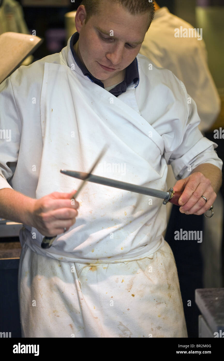 A butcher sharpens his knife in a butcher's shop in the market on the Rue Mouffetard, a celebrated food market in Paris Stock Photo