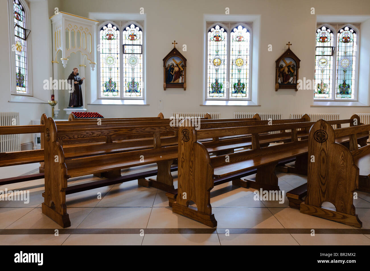 Pews, statue of St Francis of Assisi and stations of the cross in a Roman Catholic church Stock Photo