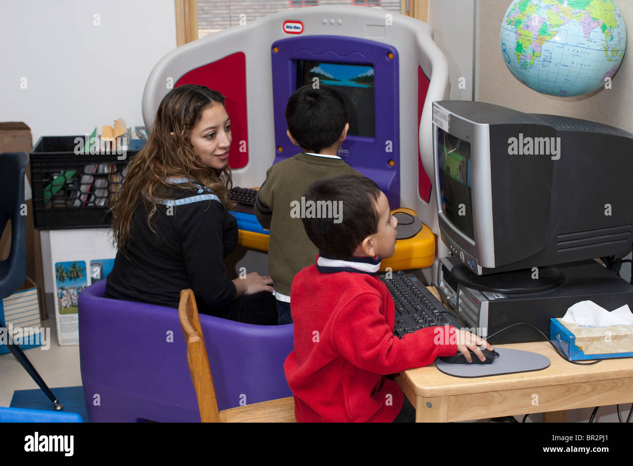 Preschool teacher and children using the computers in the classroom ...