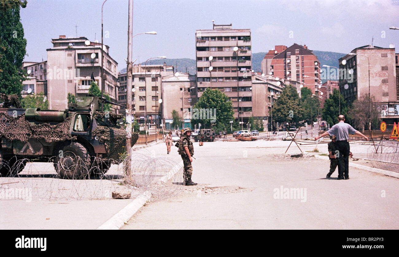 NATO troops search a man at the bridge that divides the Albanian and Serb sections of Kosovska Mitrovica. Stock Photo