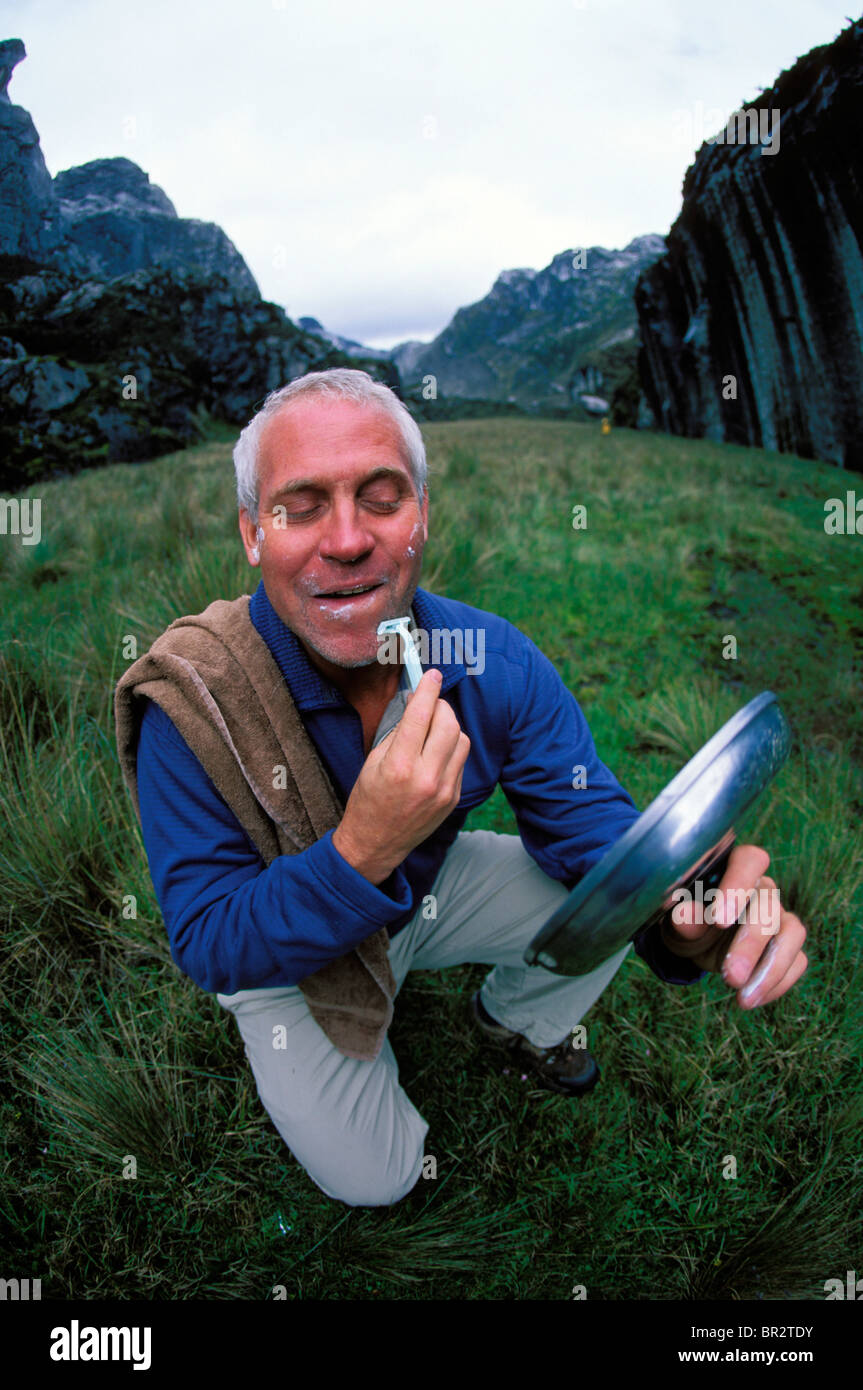 Man shaving in the mountains and using a cooking pot lid as a mirror