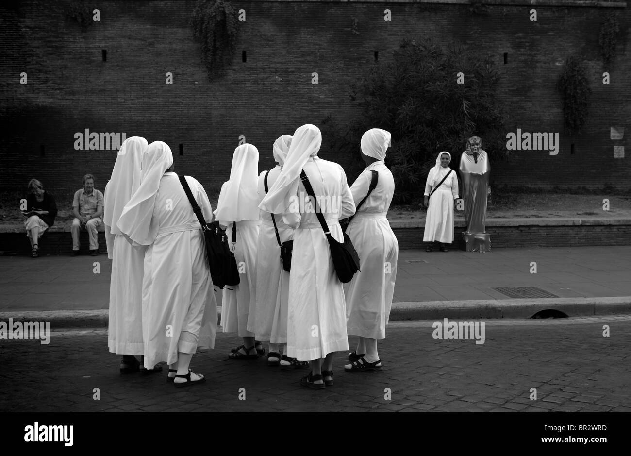 Group of nuns watching friend in street by mime artist Stock Photo