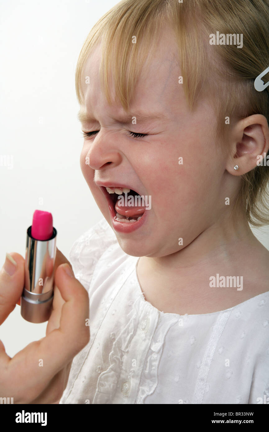 Two year old child crying with lipstick held in front of her Stock
