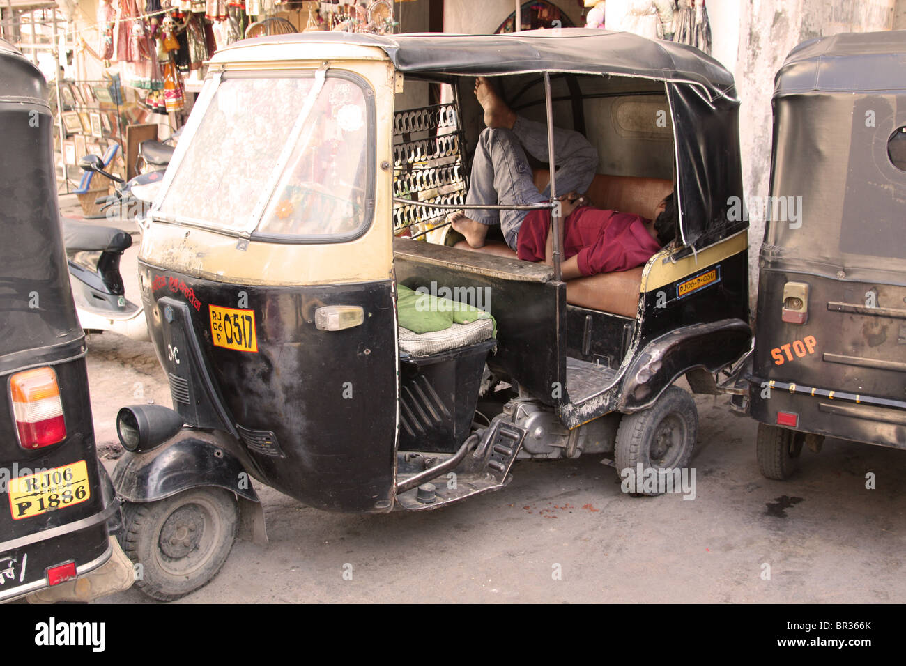 A barefoot young male Indian taxi driver sleeping on the job in the back seat of his autorickshaw. Stock Photo
