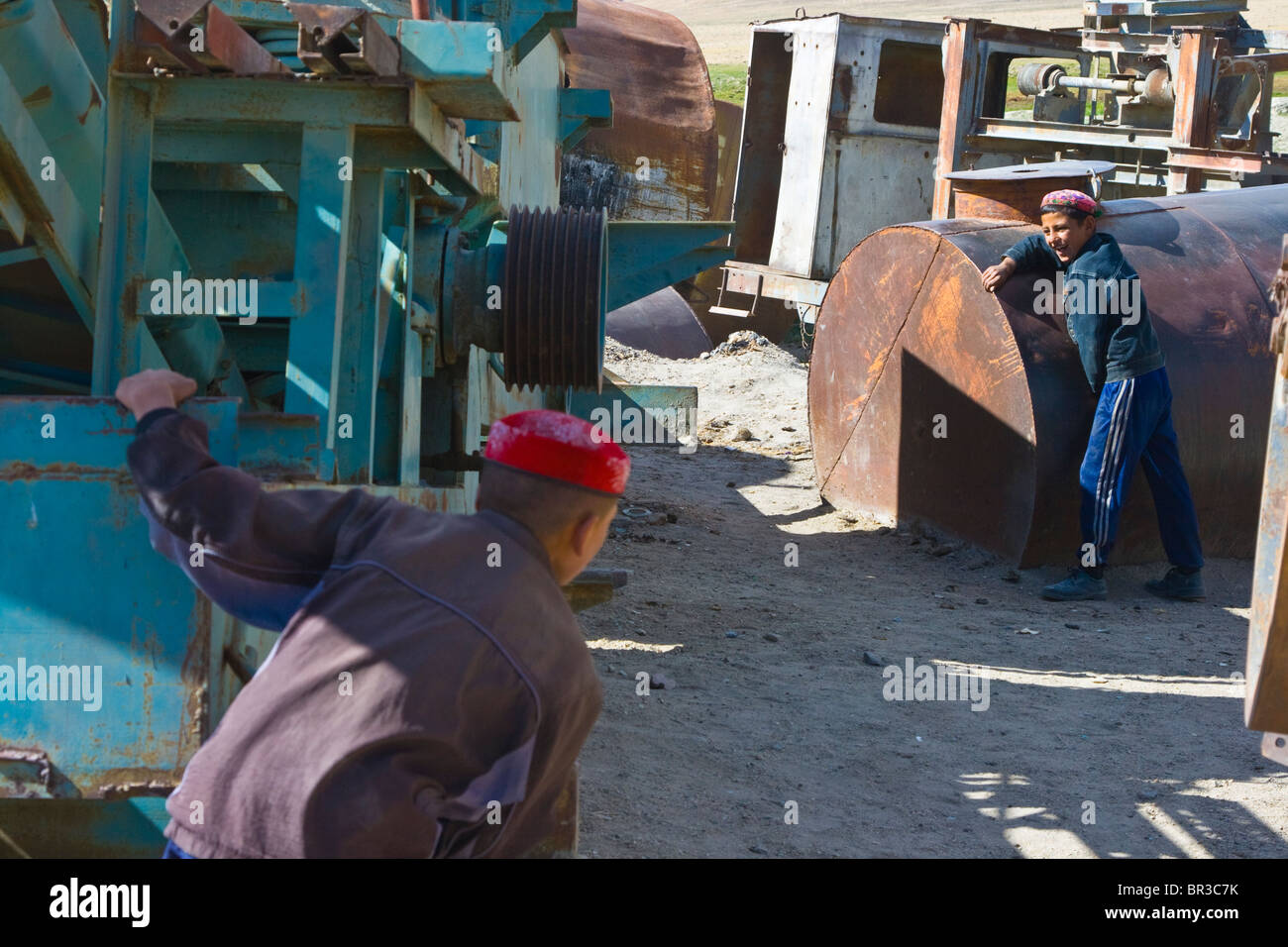 Boys playing hide n seek around rusted equipment in Bulunkul, Pamirs, Tajikistan Stock Photo