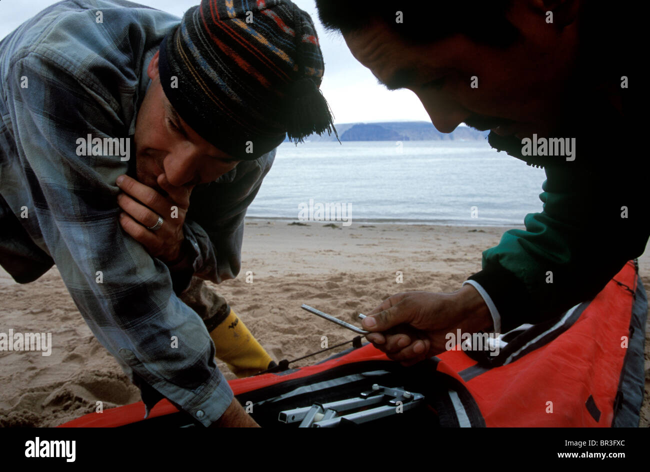 Two men work to assemble a folding kayak on a beach in Greenland Stock