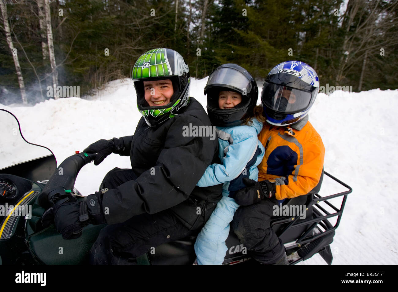 A father and his two children pose for a portrait on a snowmobile trail in Maine. Stock Photo