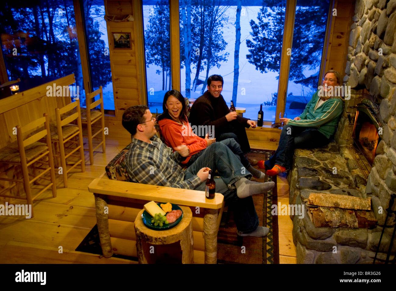 Two couples relax by the fire in a cabin in the Maine woods. Stock Photo