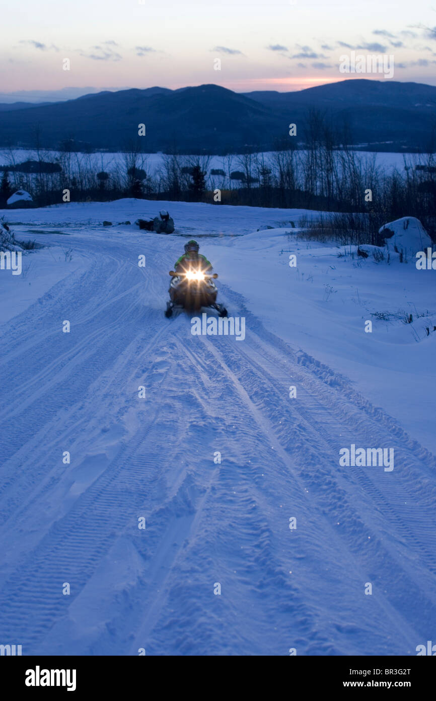 Snowmobilers speed down a trail at dusk in Maine. Stock Photo