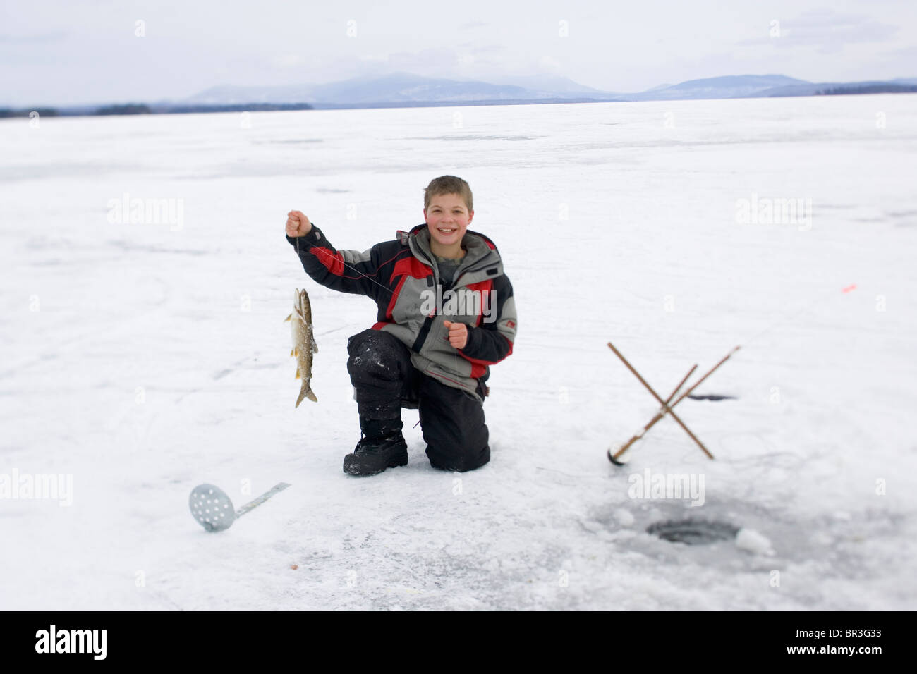 A young boy shows off a fish he just caught on a frozen lake in Maine. Stock Photo