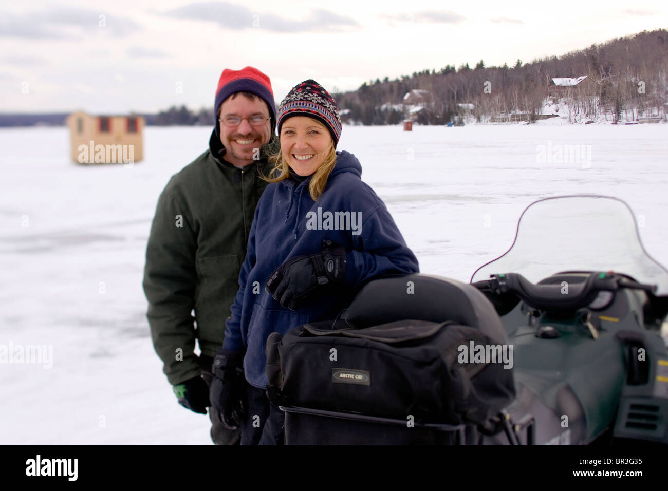 A couple pose next to their snowmobile on a frozen lake in Maine. Stock Photo