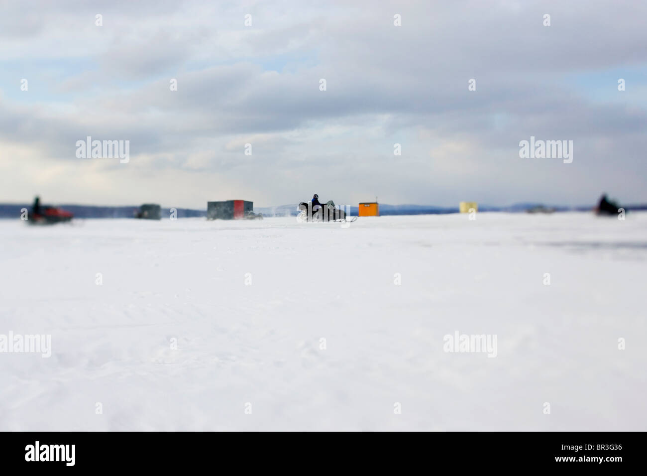 Snowmobilers speed past an ice fishing hut in Maine. Stock Photo