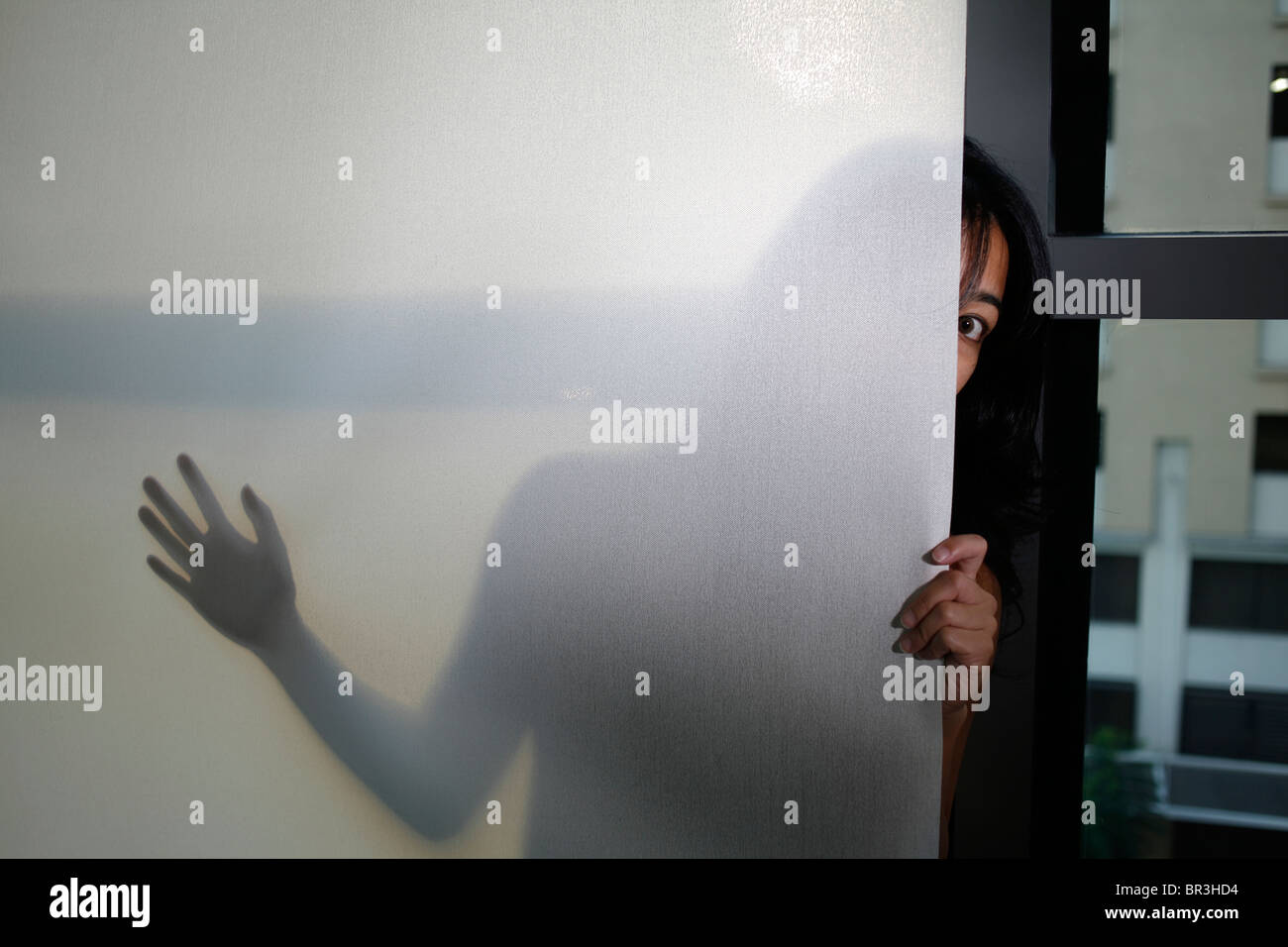 A lady peers out from behind a window shade Stock Photo - Alamy
