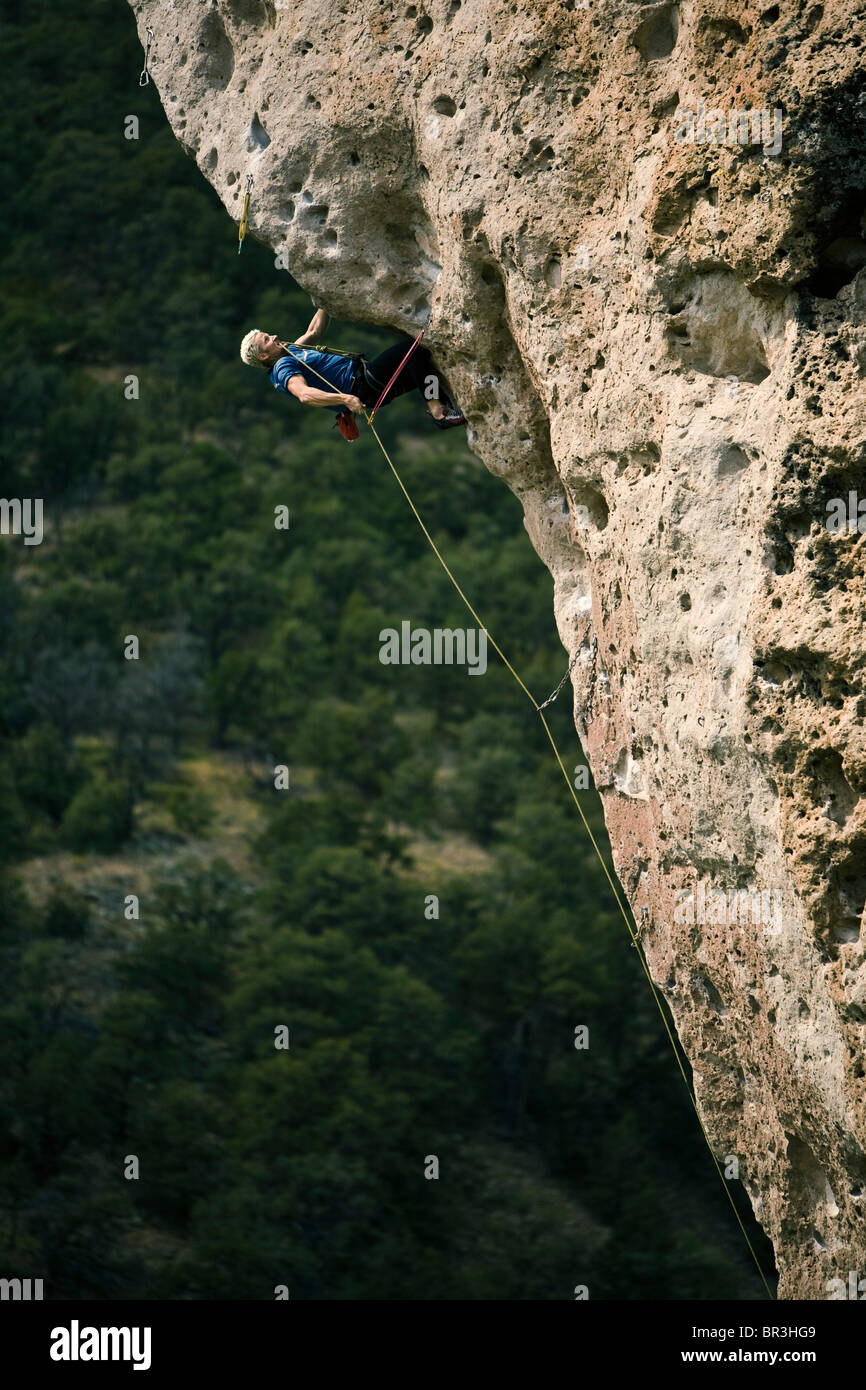 A man desperately clipping a bolt while sport climbing and overhanging