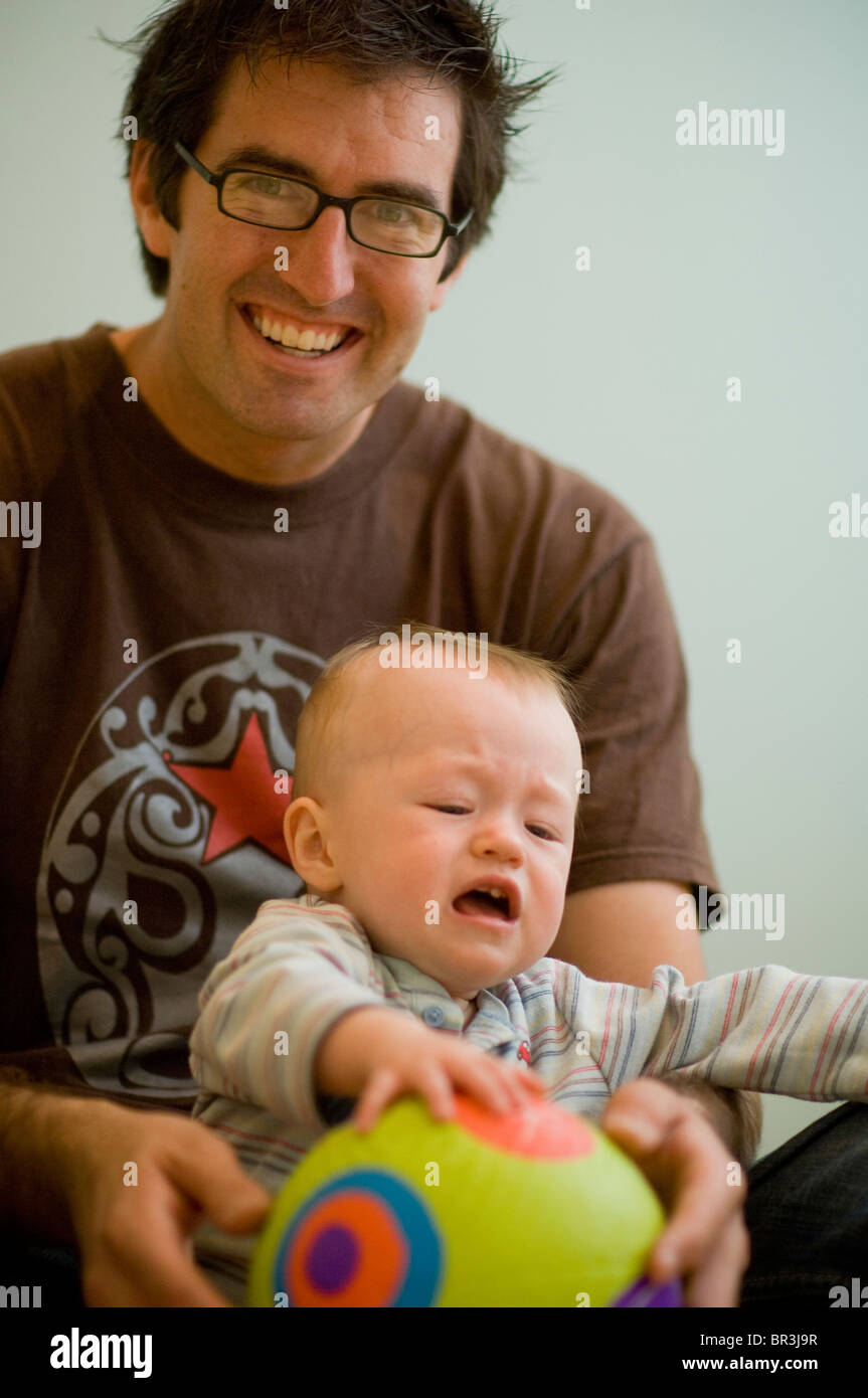 Smiling Mature Man Holds Crying Baby and Ball Stock Photo