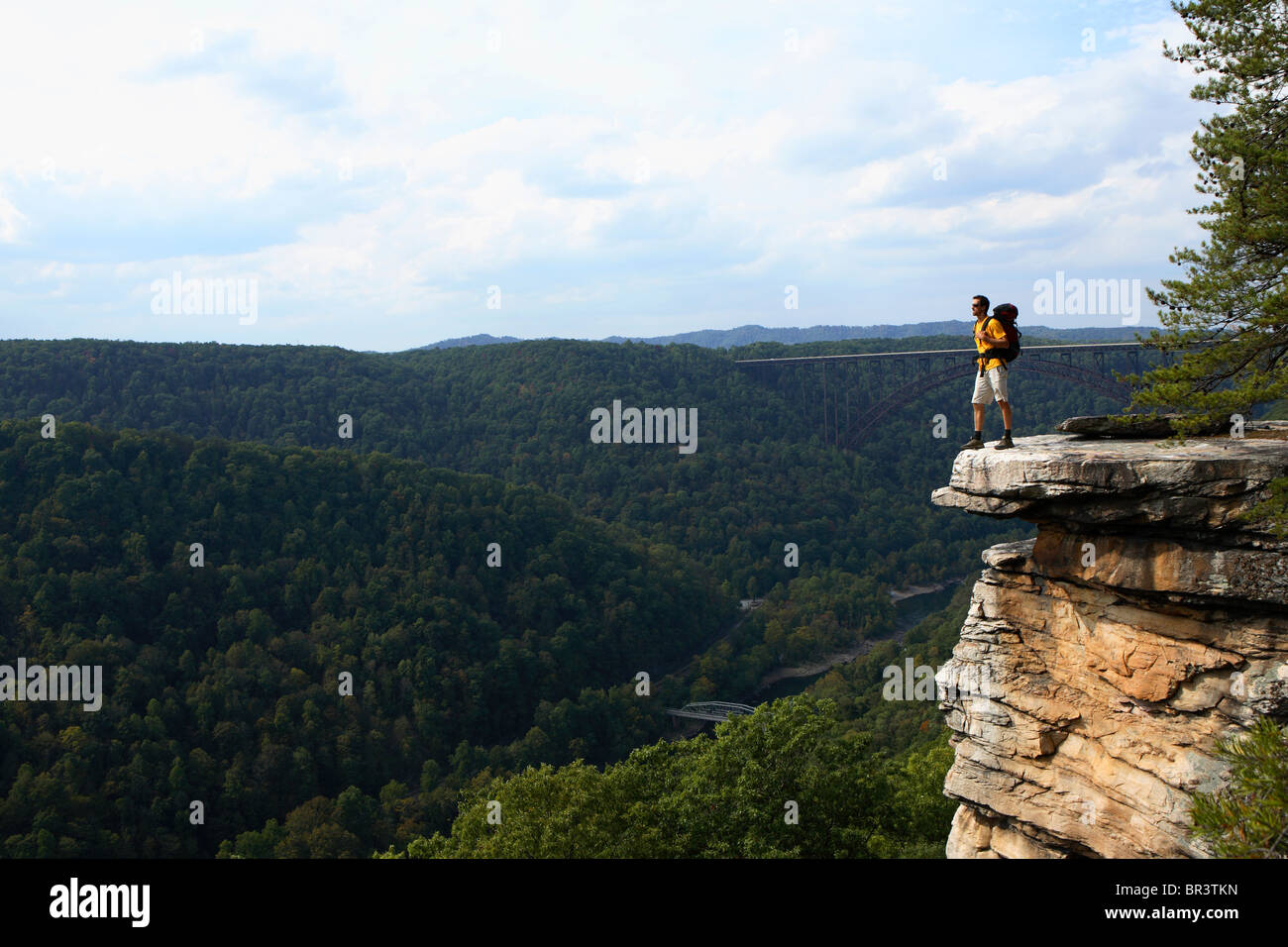 Male backpacker pauses to soak in the view from the north rim of the New River Gorge with the famous Rt 19 bride in the backgrou Stock Photo