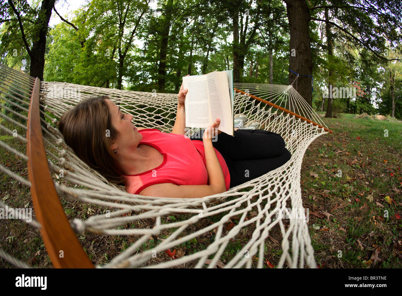 Young woman reading a good book in a hammock in her backyard in ...