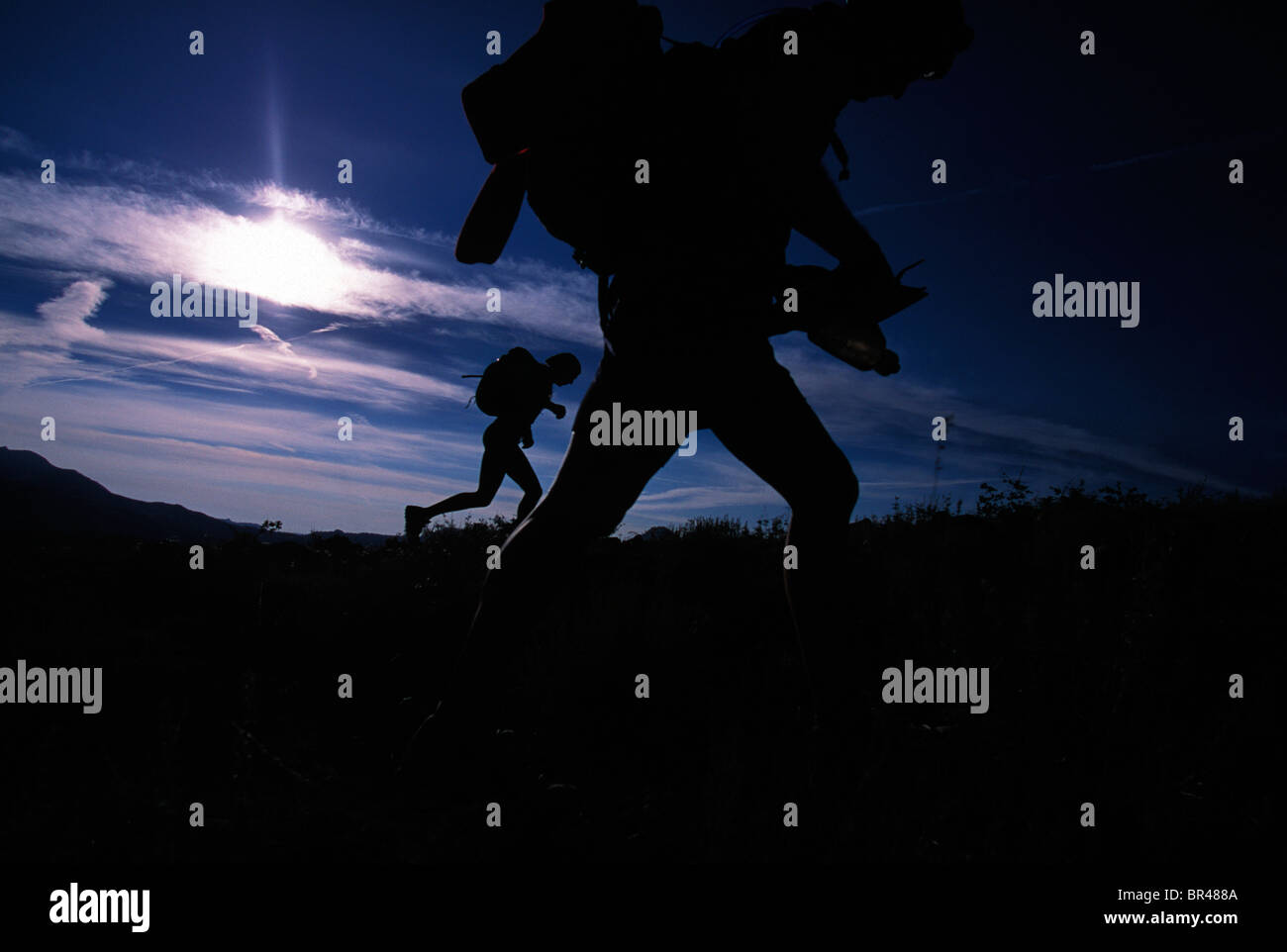 Silhouette of two people trail running in a field during an adventure race. Stock Photo