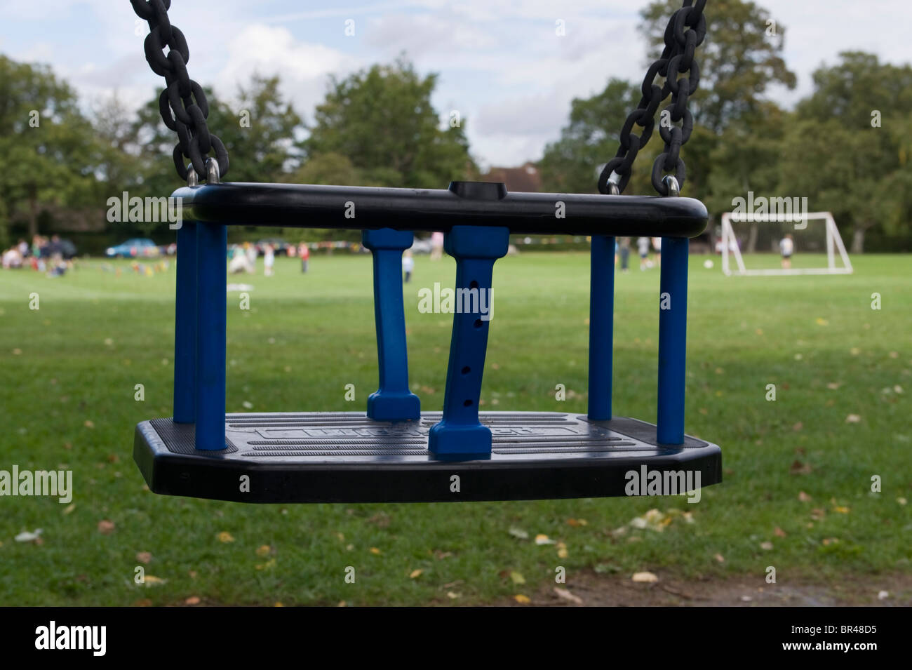 A blue child's swing seat in a children's playground on the village green in Jordans Buckinghamshire UK Stock Photo