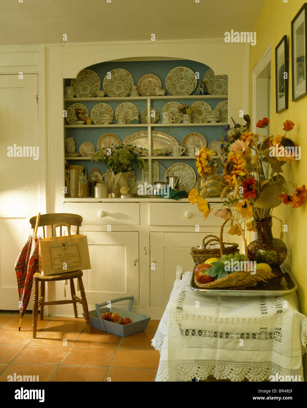 Old wooden chair beside fitted cream dresser in country kitchen with vase  of flowers on side-table with lace-trimmed cloth Stock Photo - Alamy