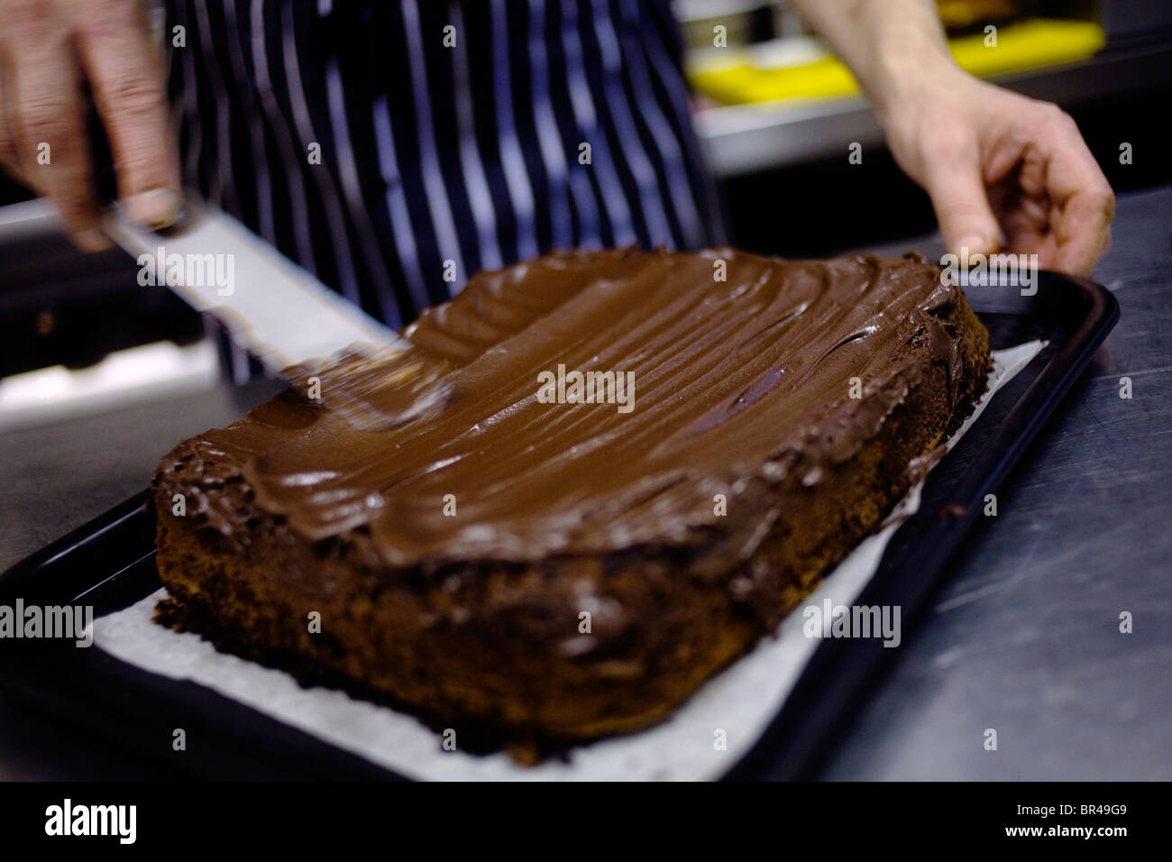 A chef giving his chocolate brownie a chocolate topping. Stock Photo