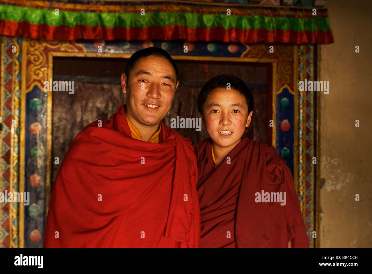 Two Tibetan monks, stand in front of an intricately carved doorway at