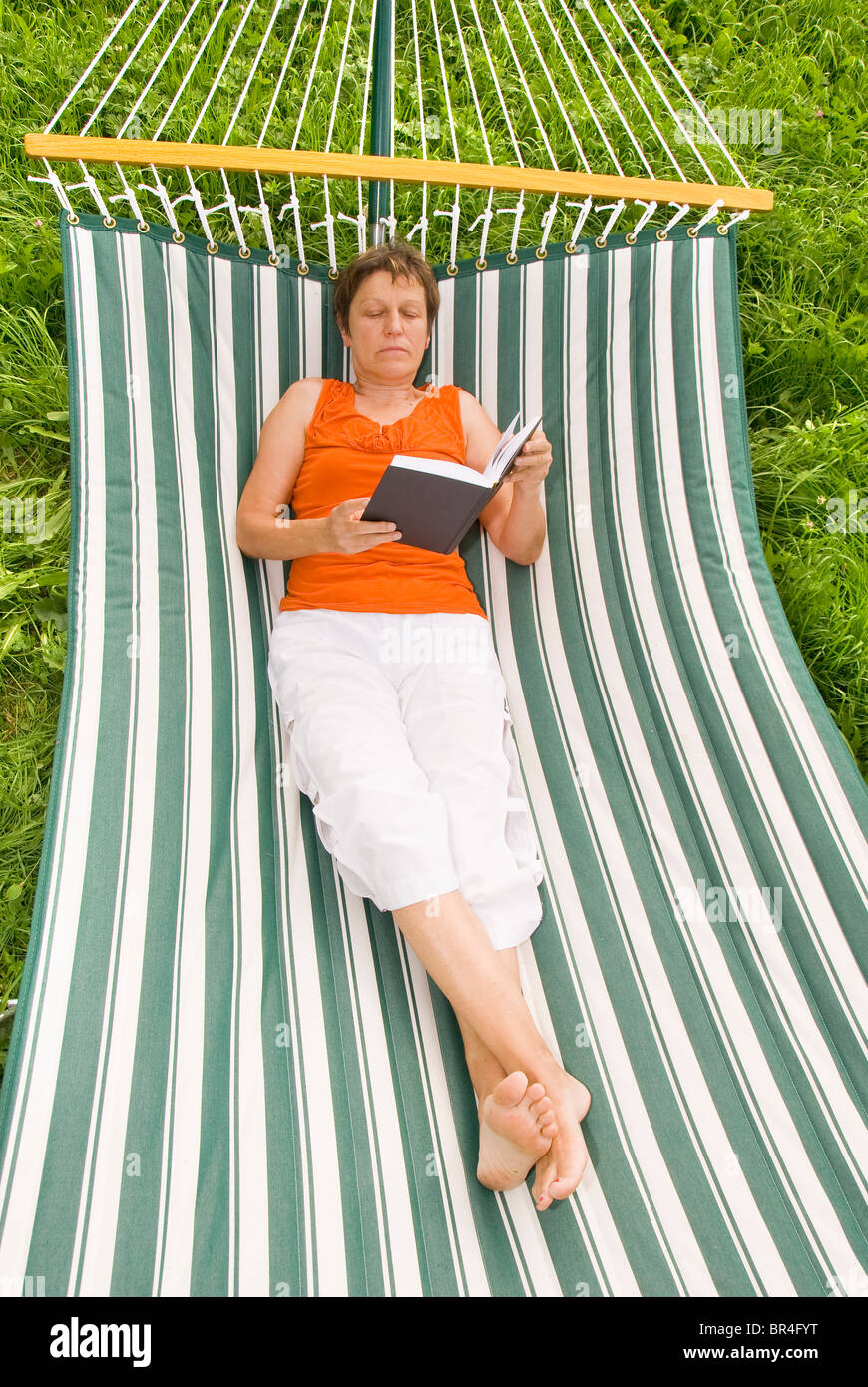 Senior woman reading a book while lying in a hammock Stock Photo - Alamy