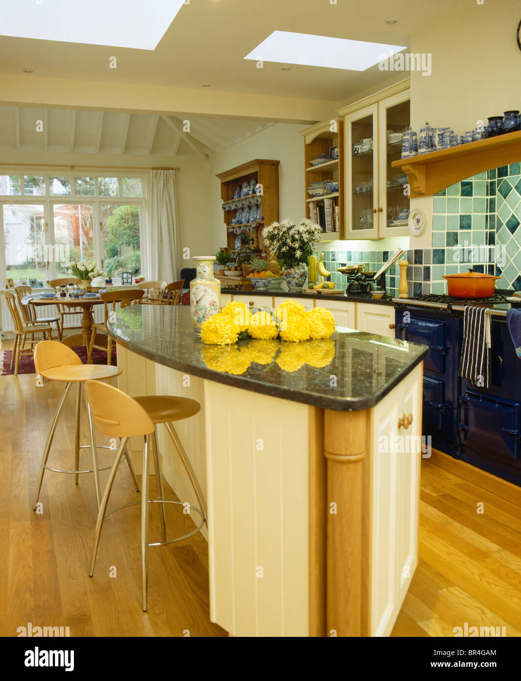 Plywood+stainlesssteel stools at breakfast bar on island unit with yellow flowers on granite