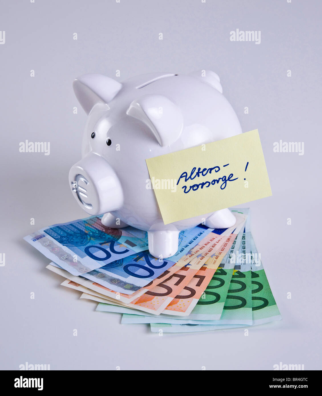 Piggy bank on bank notes, 'Altersvorsorge', pension plan written on a piece of paper Stock Photo