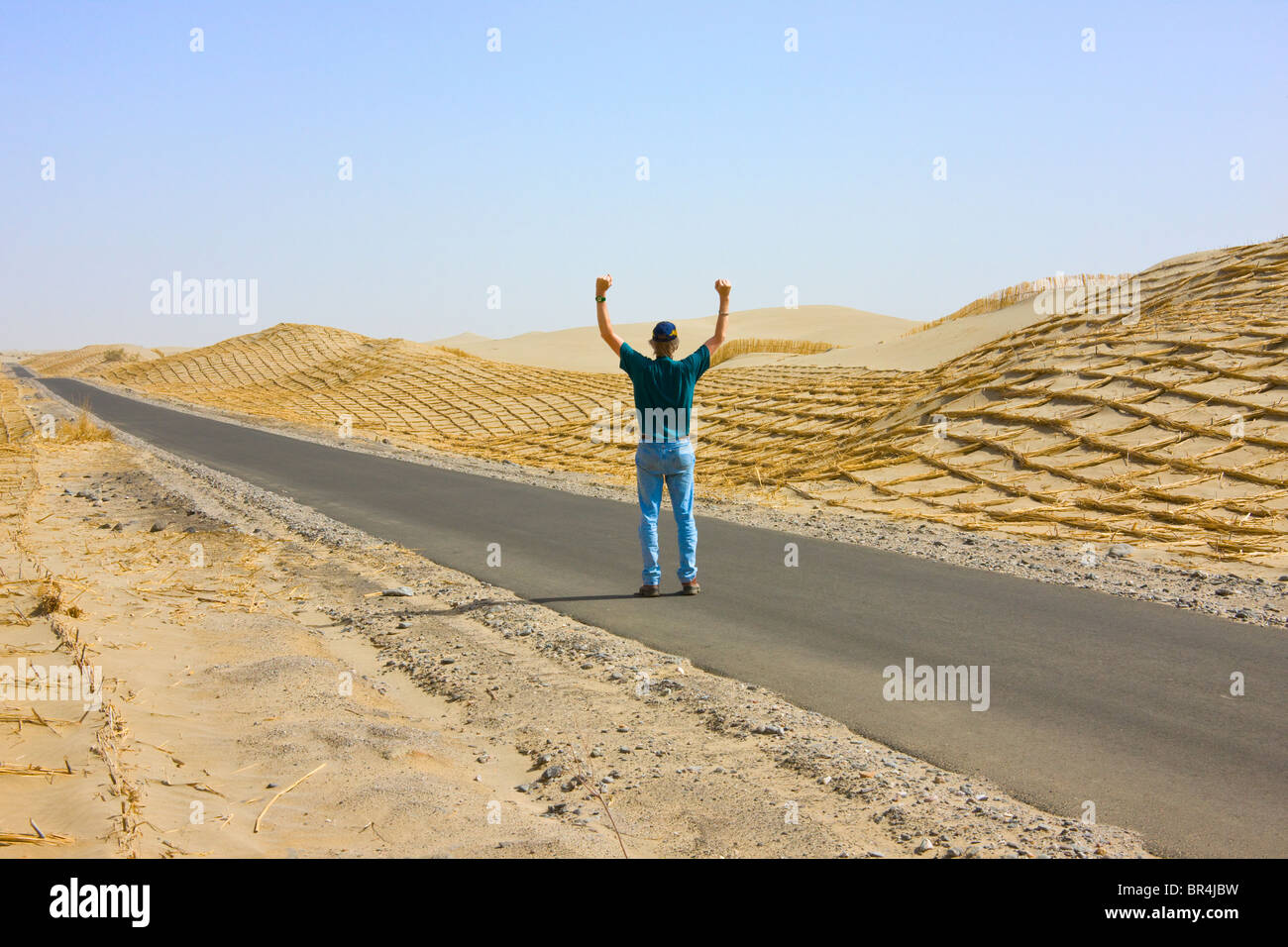 Western tourist on the freeway, reed made fence holding sand to prevent desertification along the freeway, Aksu, Xinjiang, China Stock Photo