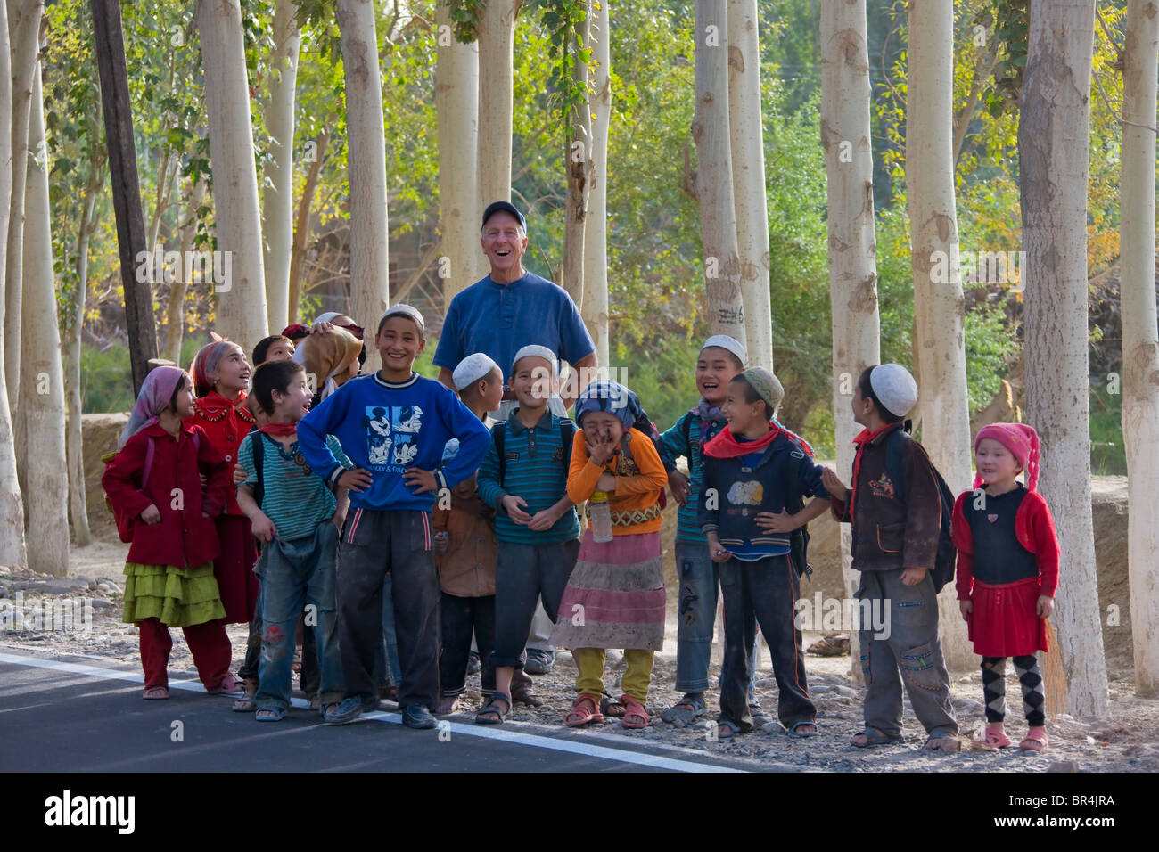 Western tourist with Uighur children in front of poplar trees, Hotan, Xinjiang, China Stock Photo