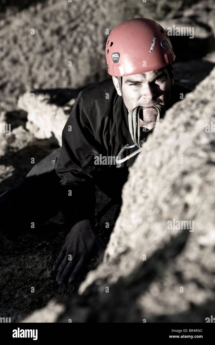 A rock climber looking towards the bolt with a quick draw in his mouth