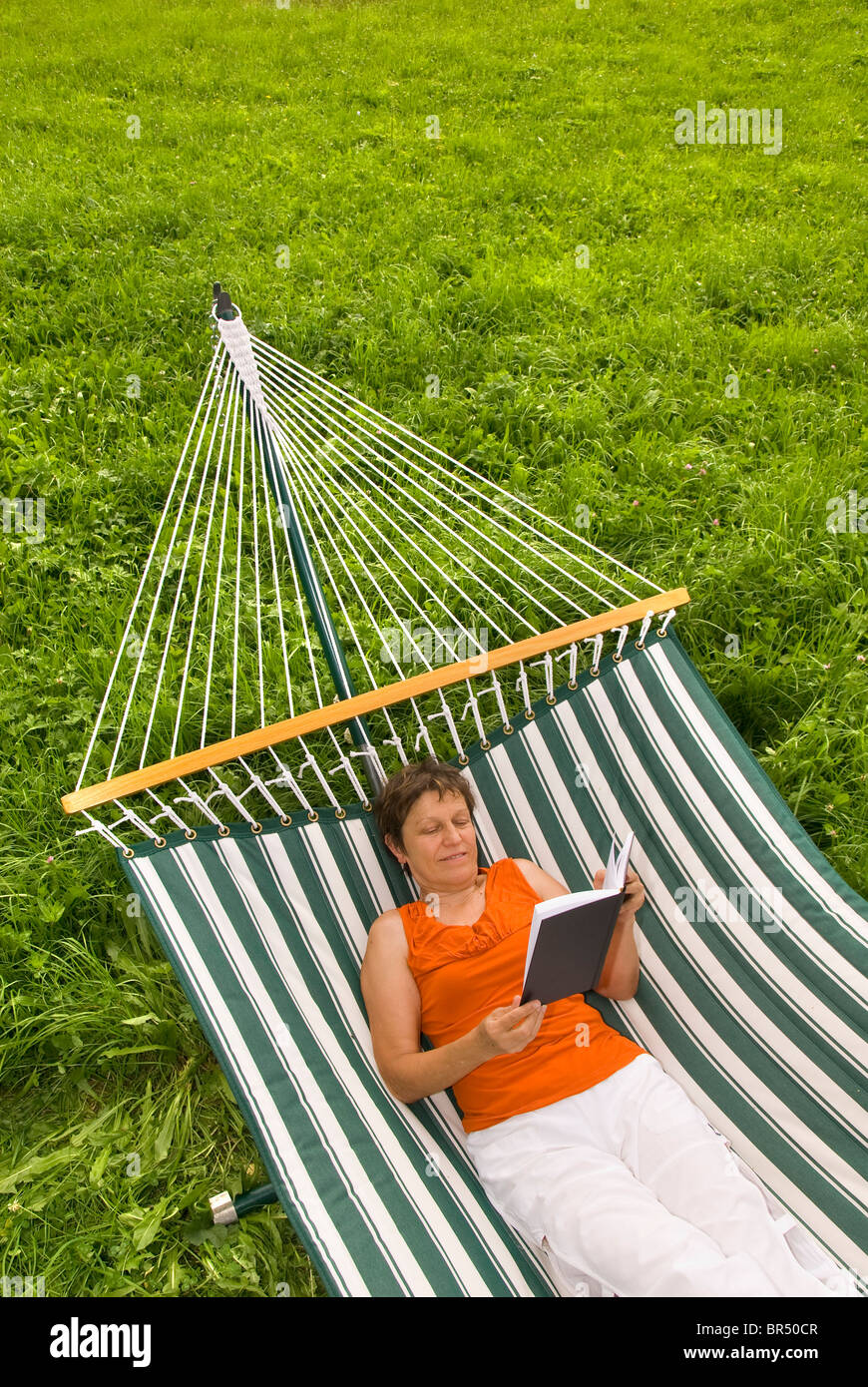 Senior woman reading a book while lying in a hammock Stock Photo - Alamy