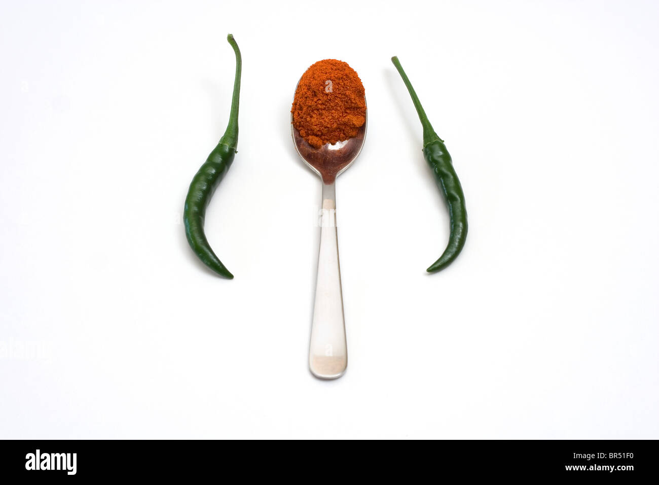 Teaspoon of red chilli powder and two green chillies on a white background Stock Photo
