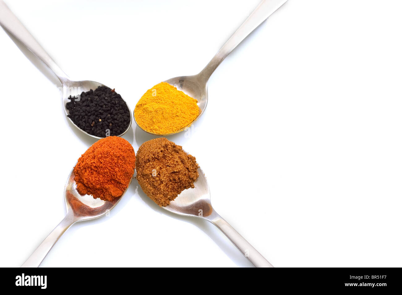 Teaspoons of spices commonly used in Indian cooking, coriander, tumeric, onion seeds and chilli powder, on a white background Stock Photo