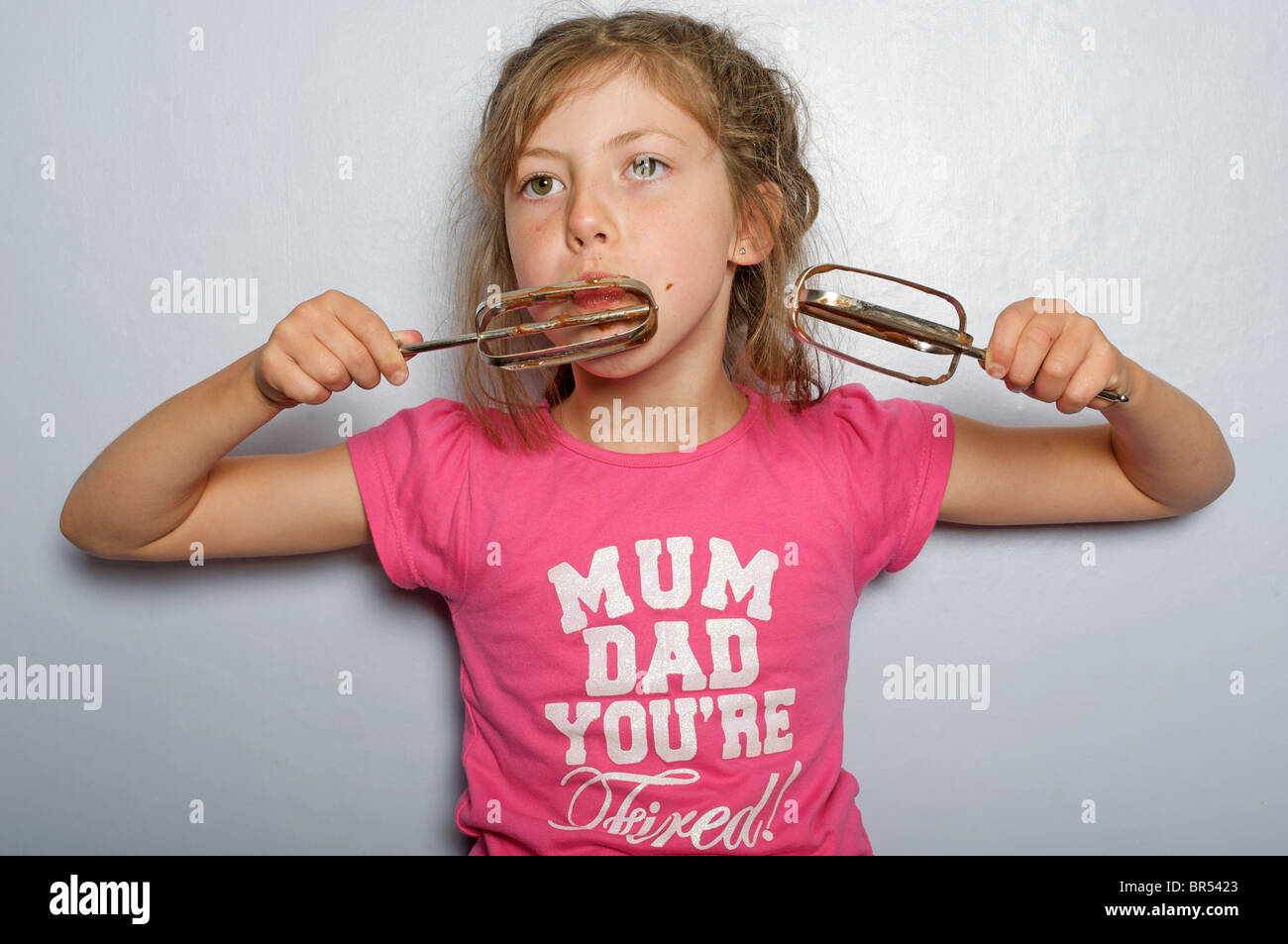 Young girl eating chocolate icing off a whisks Stock Photo Alamy