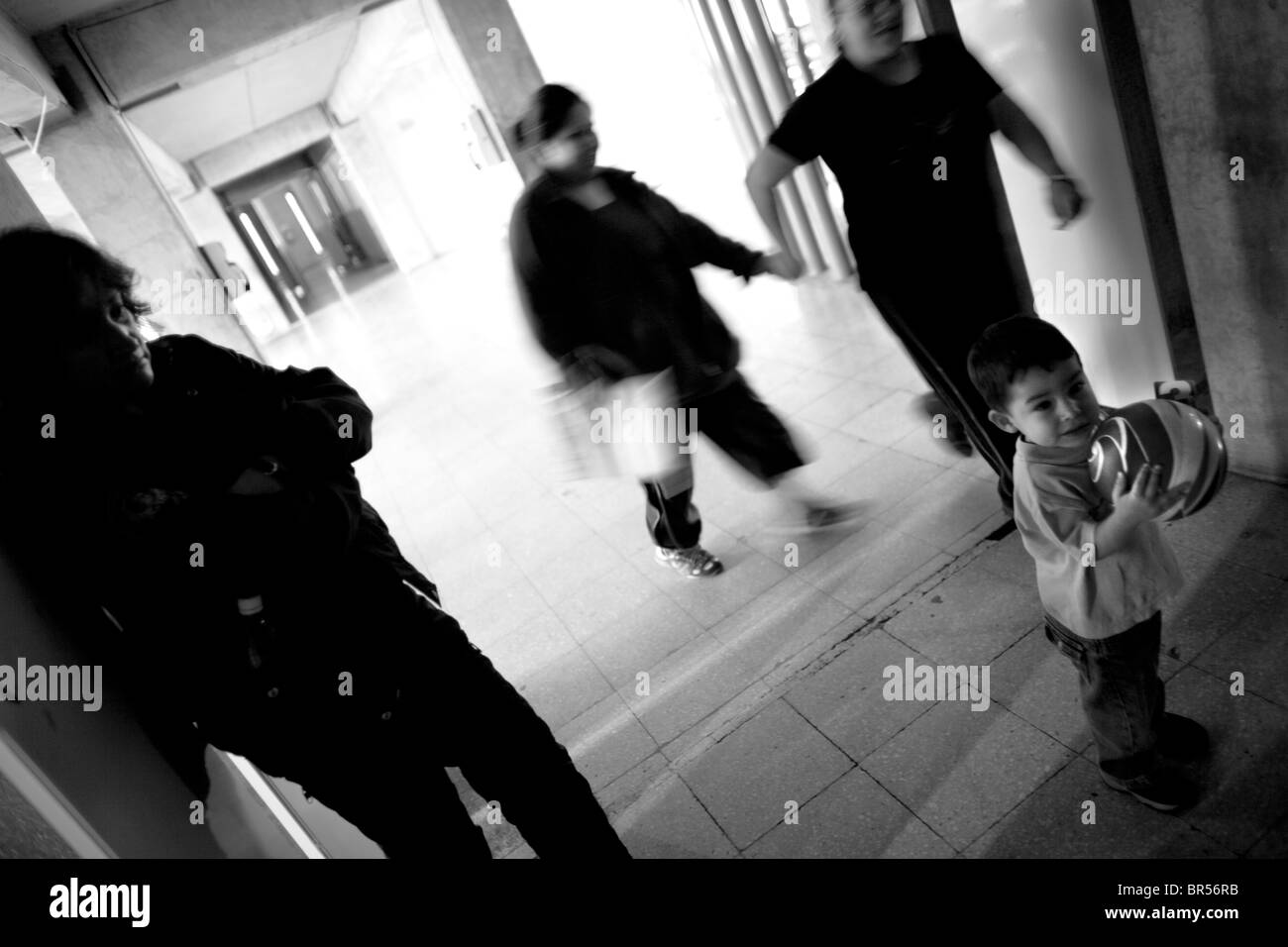 A child plays with a ball in a prison hallway while a guard watches. Stock Photo