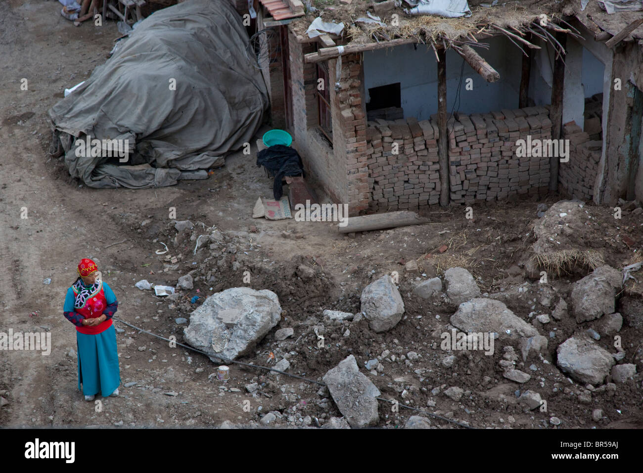 Young Tibetan woman in traditional dress standing by a house under construction in Xiahe Gansu China. Stock Photo