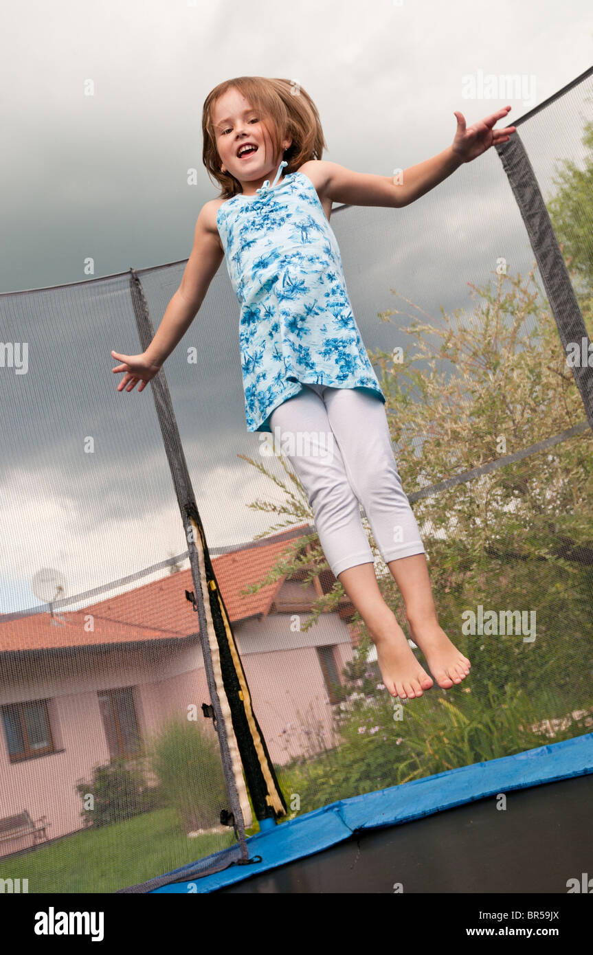 Small cute child jumping on trampoline - garden and family house in background Stock Photo