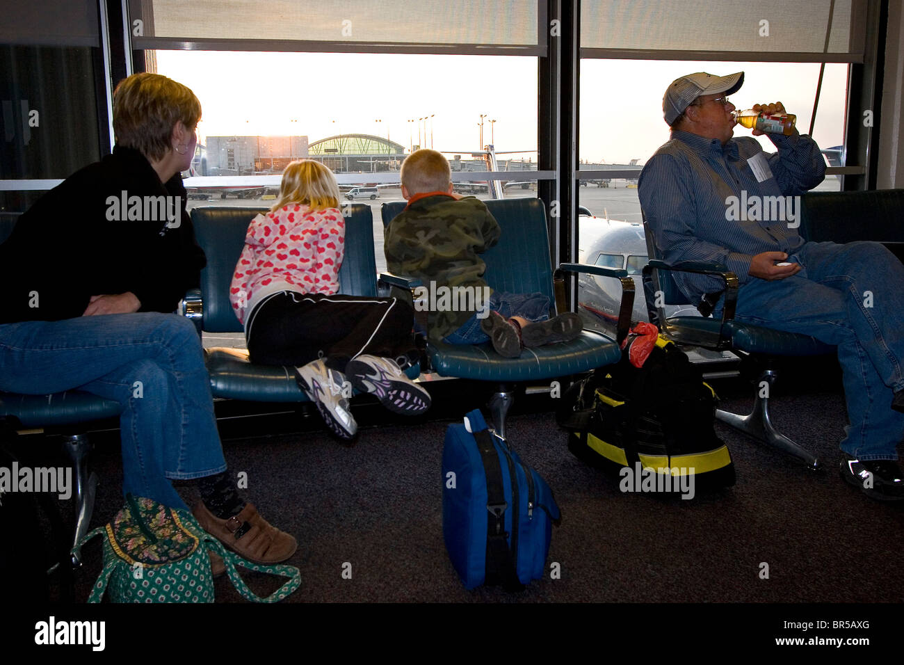 Family of four in airport waiting for their flight at the gate window at sunrise Stock Photo