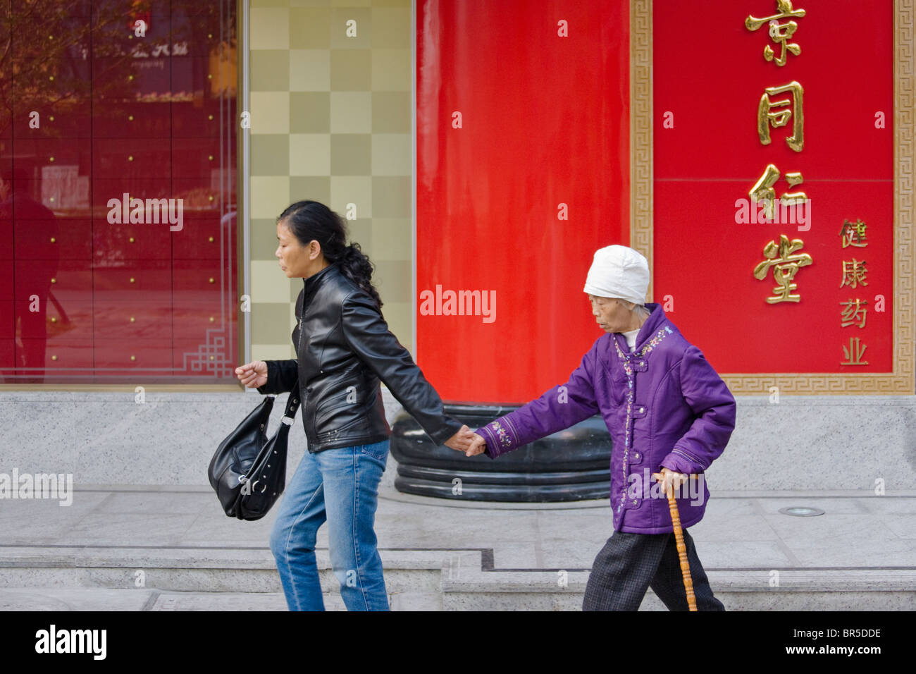 Young woman hand in hand with older woman with walking stick on the street, Chengdu, Sichuan, China Stock Photo