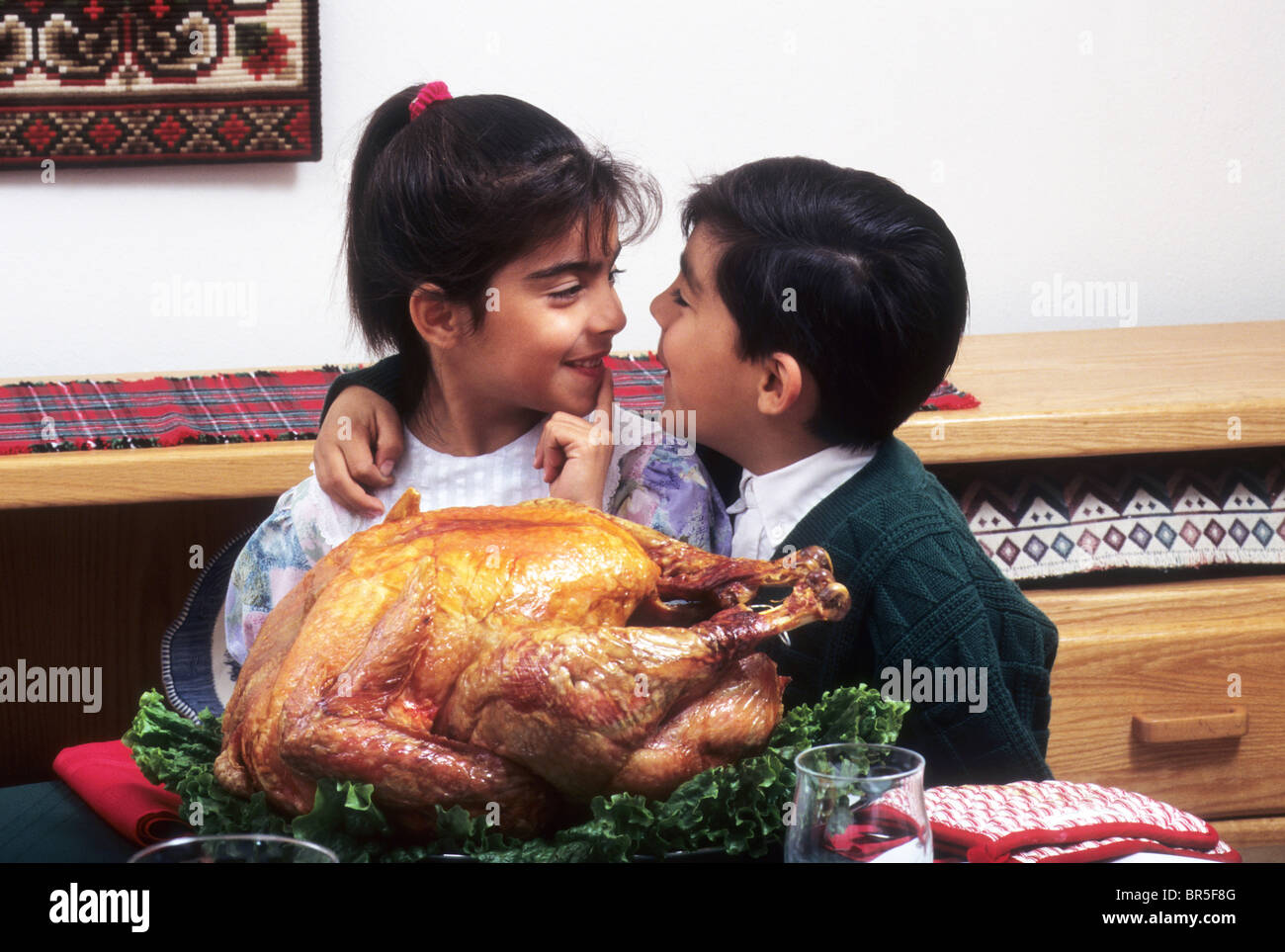 Hispanic twin boy and girl tease each other before eating turkey dinner ...