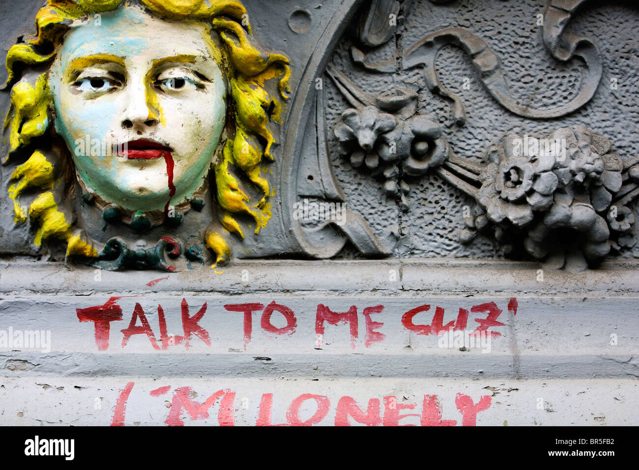 Part of a facade of a house in New York, with an antique sculpture and a writing 'Talk to me cuz' I'm lonely' Stock Photo