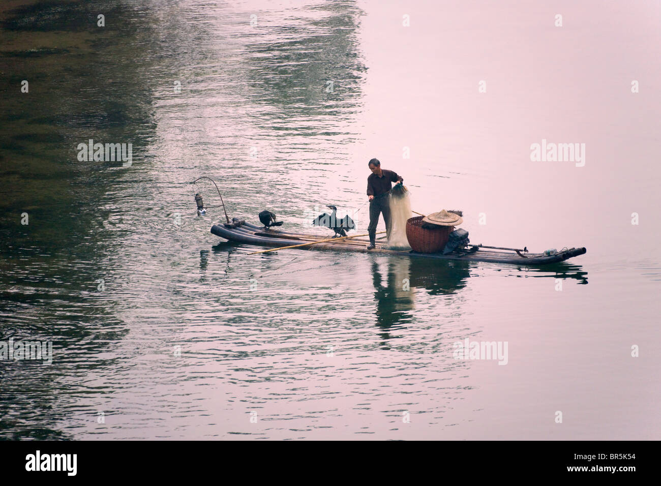 Fisherman casting fishing net on bamboo raft on Li River, Yangshuo, Guangxi, China Stock Photo