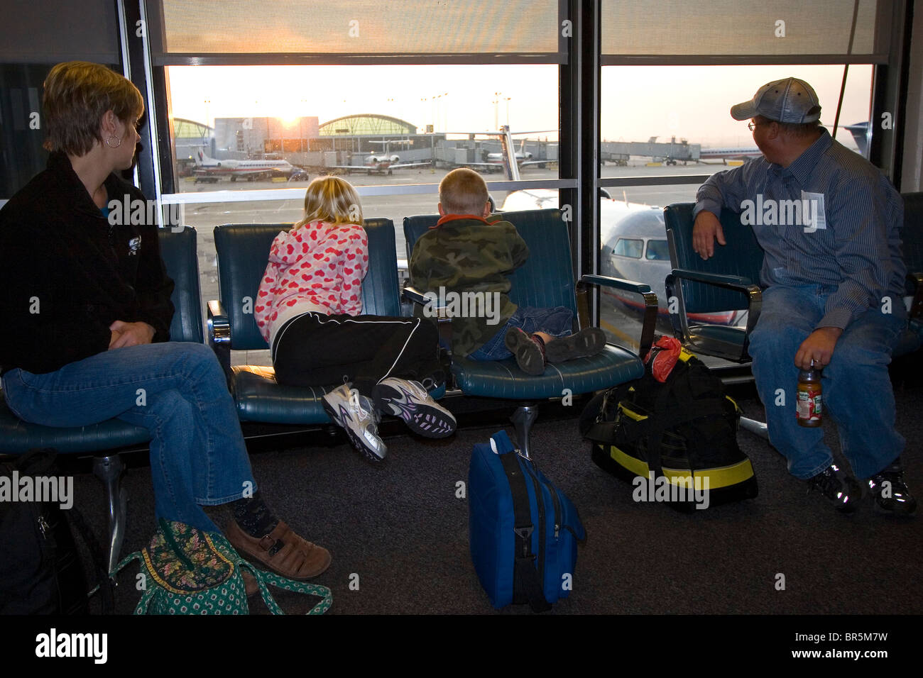 Family of four in airport waiting for their flight at the gate window at sunrise Stock Photo