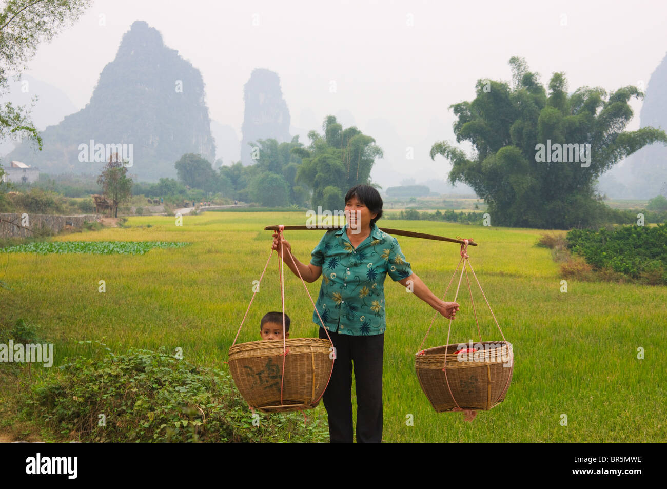Woman carring child in basket using shoulder pole, Yangshuo, Guangxi, China Stock Photo