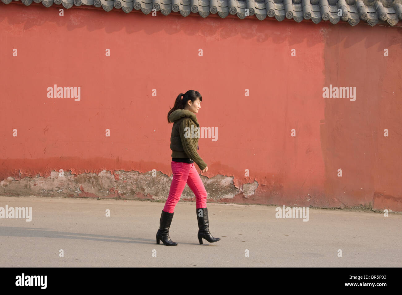 Girl wearing high heels passes by red wall of temple, Chengdu, Sichuan, China Stock Photo