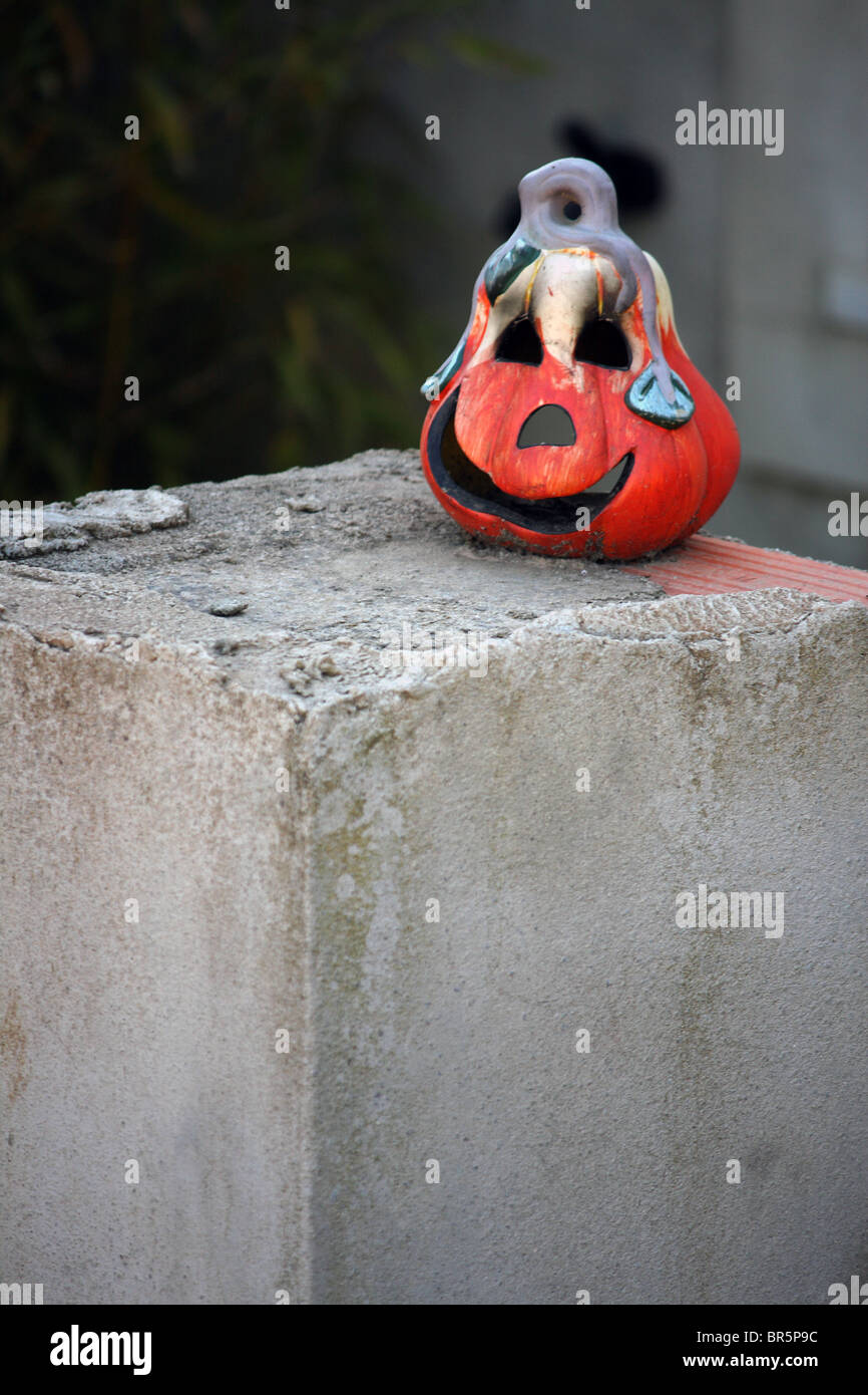 A melted Halloween pumpkin with wax dripping down it, sat outside on a concrete pillar Stock Photo