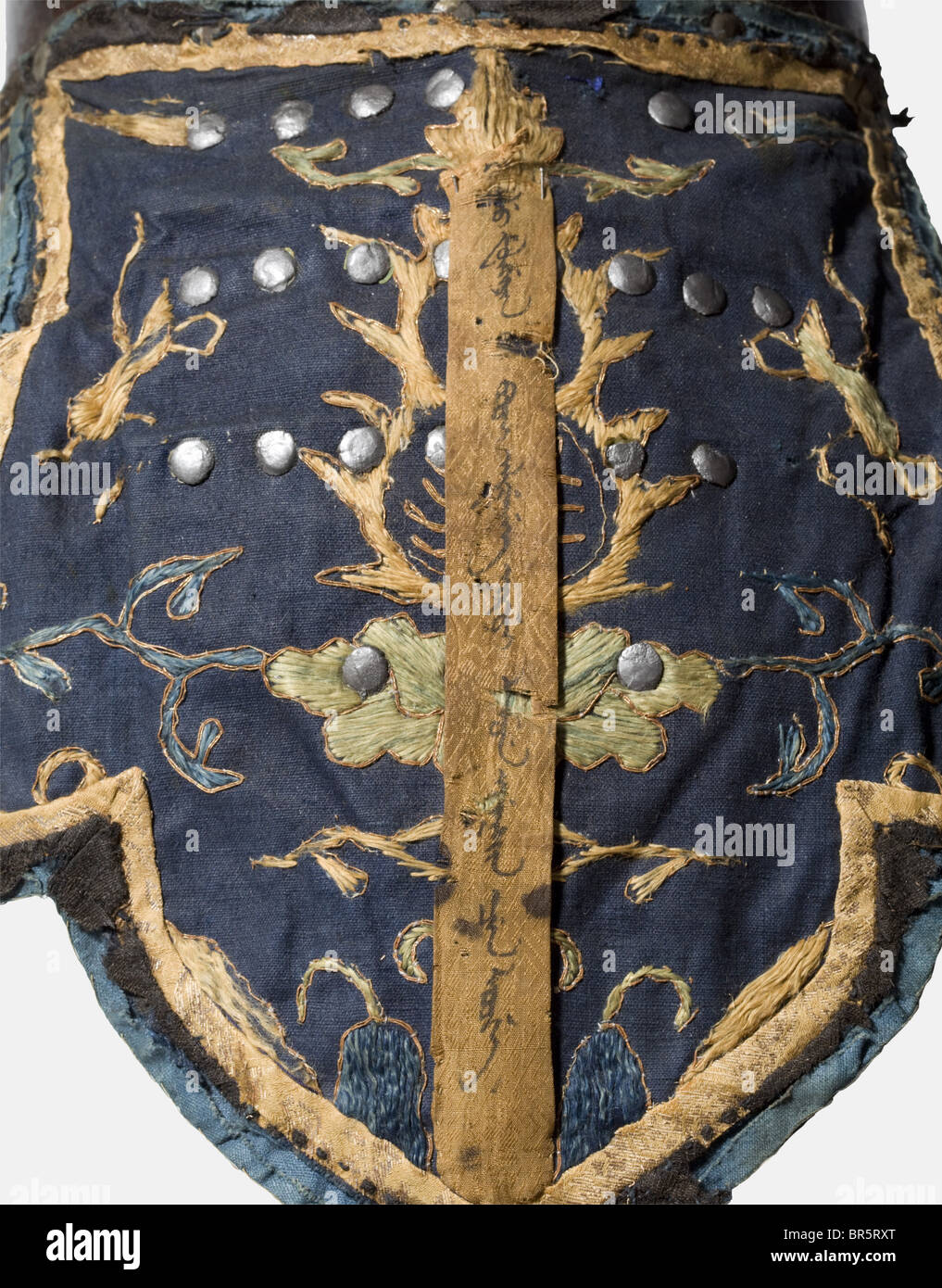 An Chinese officer's helmet (niru), Qing Dynasty, 17th/18th century Two-piece, brass soldered iron skull with riveted crown and tall, slender plume socket (screwed, but loosened), likewise riveted rim with curved peak. Cheek-pieces made of fabric and riveted to the skull, cheek guards and neck guard with riveted metal plates(!), additionally covered with dark blue cloth decorated with polychrome silk embroidery and bordered with silk brocade, the surrounding piping of black horse hair. The neck guard surmounted by a heavily worn silk band with the name and rank, Stock Photo