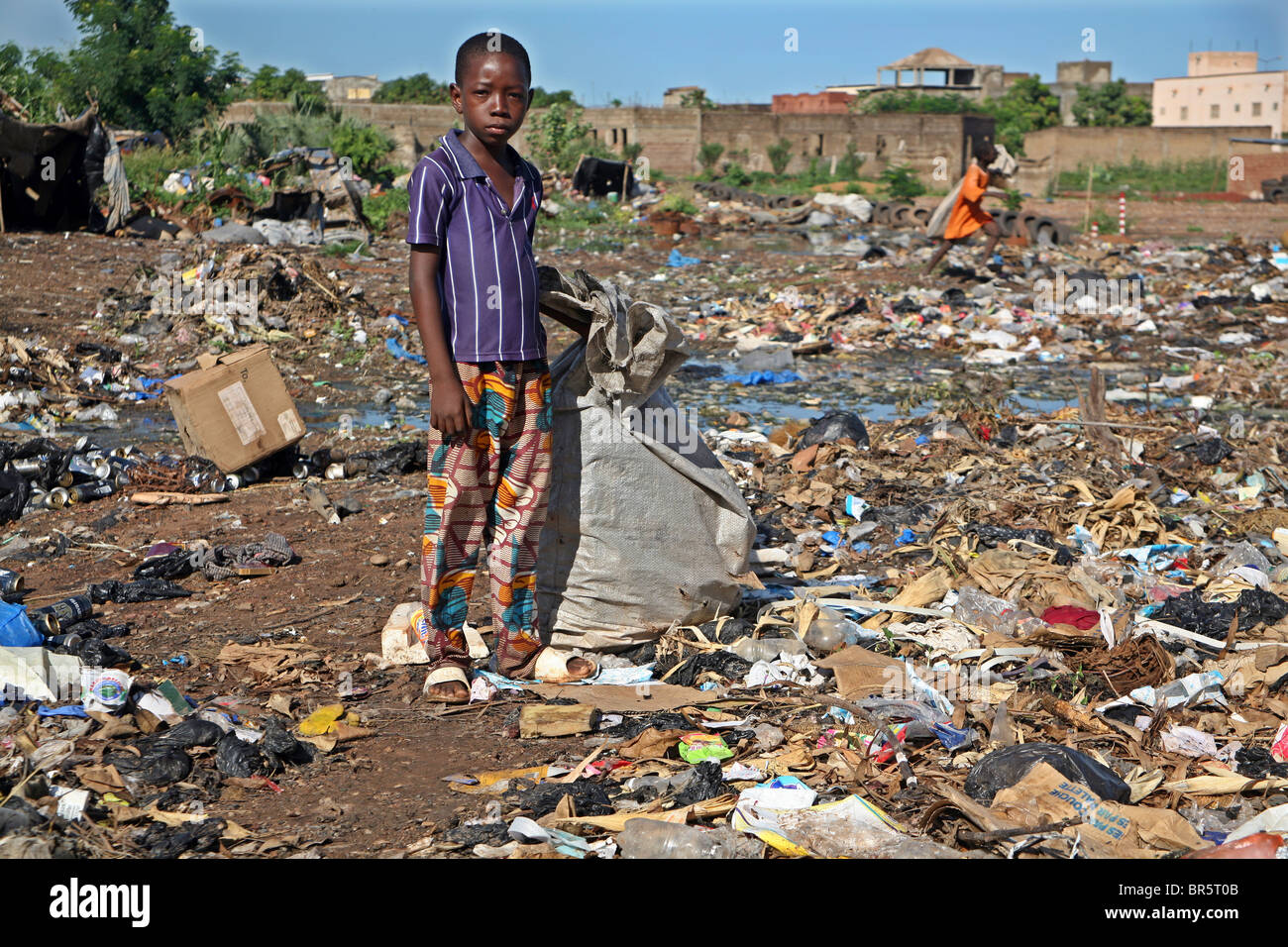 A young boy scavenges through a waste dump looking for anything plastic that he can sell for recycling, Bamako, Mali. Stock Photo